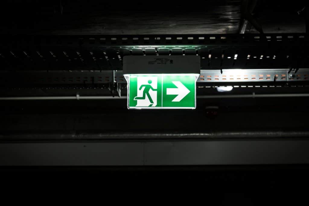 pexels-photo-878832-878832 Bright green emergency exit sign with arrow in a dark industrial setting, indicating evacuation route.